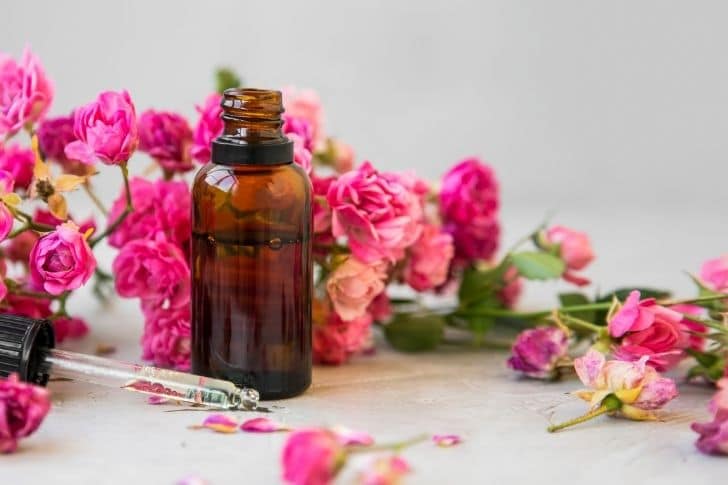 Botellita con aceite de rosas junto a pétalos de rosas.